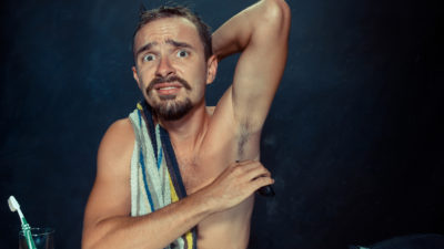 Photo of a frustrated handsome man shaving his armpit